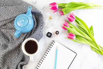 tea kettle with a cup on a table with notebook pencil and flowers. Used for a blog post on blogging tips for newbies