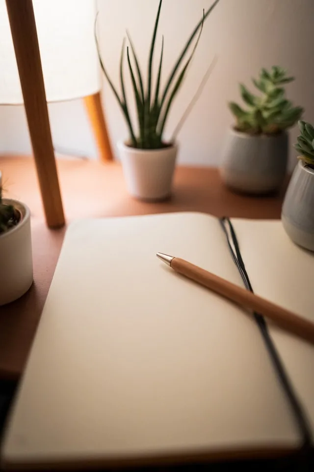 A notebook with a pen on it and surrounded by green plants. used for a blog post on Sell Short Stories for Money