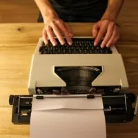 A table with a typewrite on it and someone typing. Used as a blog graphic for a blog post on Sell Short Stories for Money
