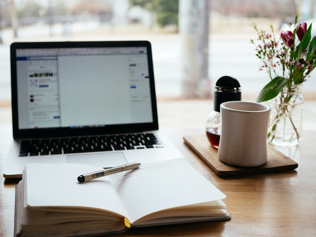 A table with a book, coffee mug and a laptop. Used for a blog post on Sell Short Stories for Money