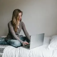 women sitting on the bed with the laptop. Used as a image for a blog post on how to make money typing names online