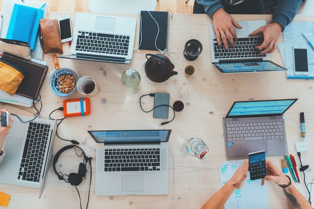 a table with multiple laptops on it with other electronic accessories. graphic for a blog post on Get Paid To Promote Links