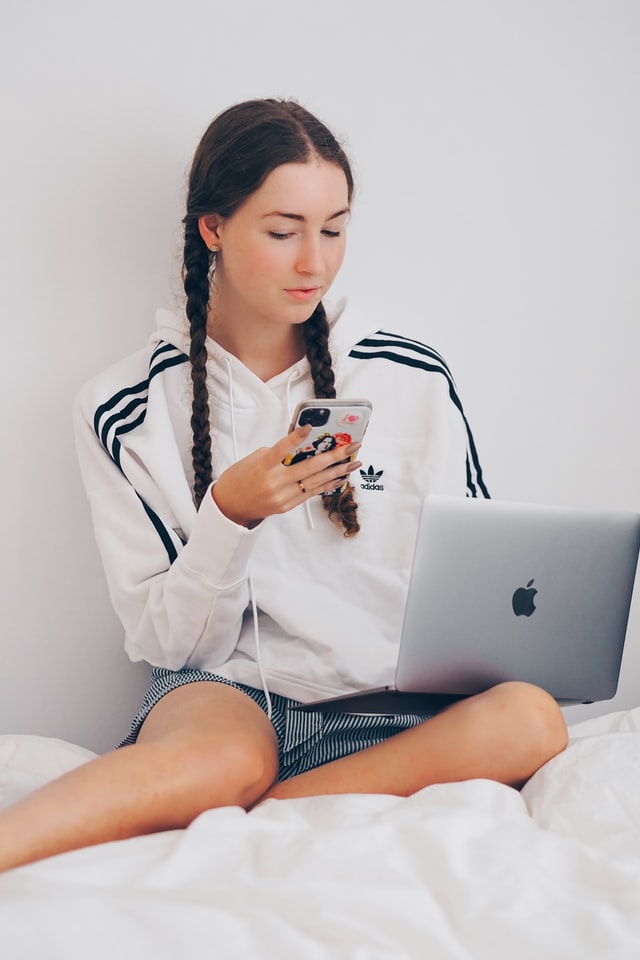 girl sitting on a bed with laptop on the lap and phone in the hand. Blog graphic on How to make money as a teenager without a job