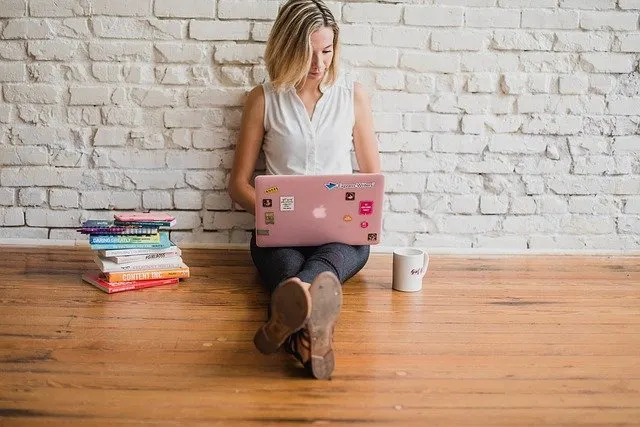 women sitting on the floor with a laptop on her lap and books kept to the left. blog picture for Online Typing Jobs Without Investment