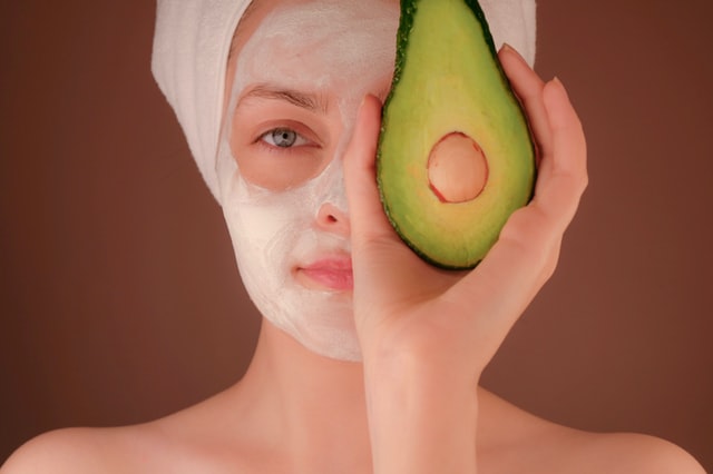 Women with a faceoack and hiding an eye with a cut up avacado. Graphic for a blog post on skin care business name ideas