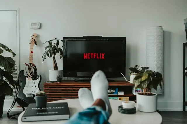 This image shows that someone is watching Netflix on TV. It also has guitar kept next to tv. Graphic used on a post on how to get paid to watch tv