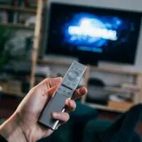 This image shows that someone is watching TV. Using remote to change the channels. Graphic for a post on getting paid to watch tv