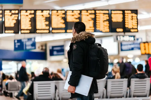 In this post a man is watching the flight schedule on the screen at the airport. graphics used for a post on How to become a travel agent from home