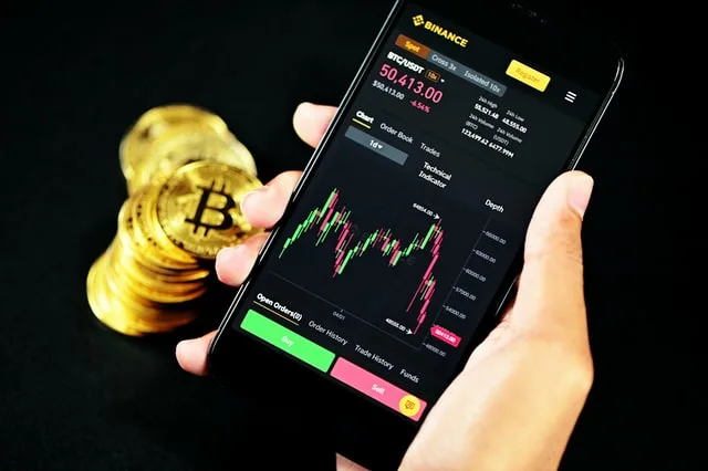 In this image someone is watching trading on his phone with some bitcoins alongside