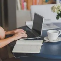table with laptop, coffee mug, books and hands