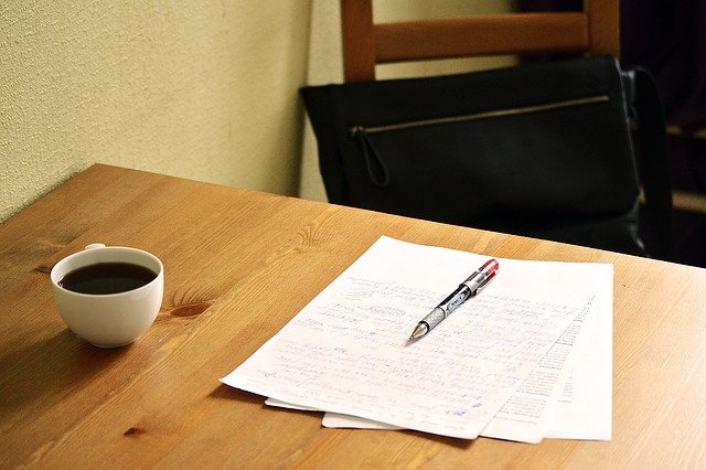 A table with papers on it, a pen and a coffee cup.