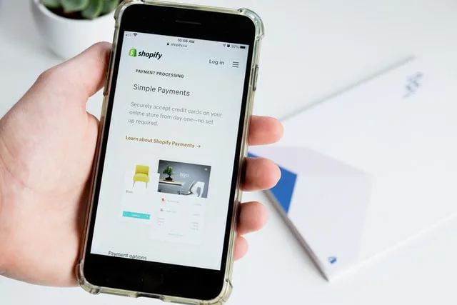 In this image there is a phone with shopify on it. Image for a post on selling locally