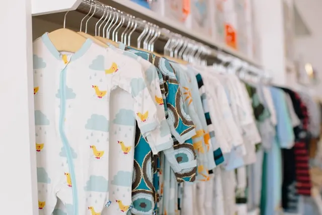 In this image a wide variety of rompers are hanged on a rod.