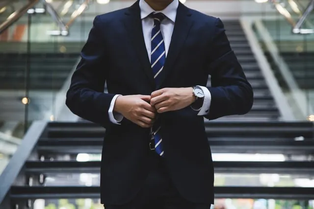 In this image a gentleman is standing in his corporate attire while adjusting his suit