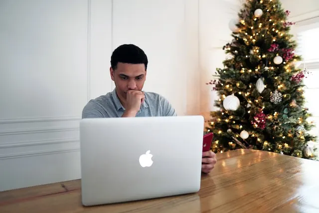 a man working ona desk with apple laptop with a christmas tree behind