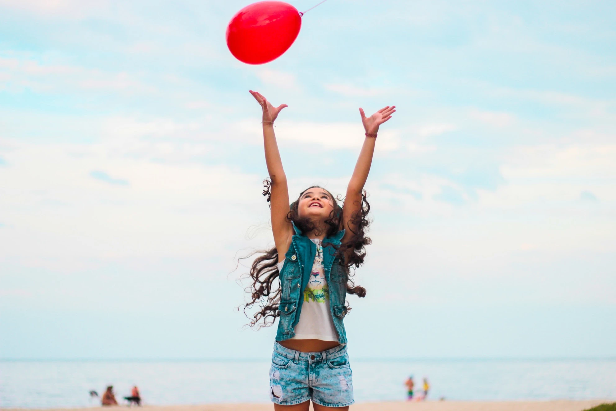 A 10 year old on the beach jumpimg tp grab a red baloon