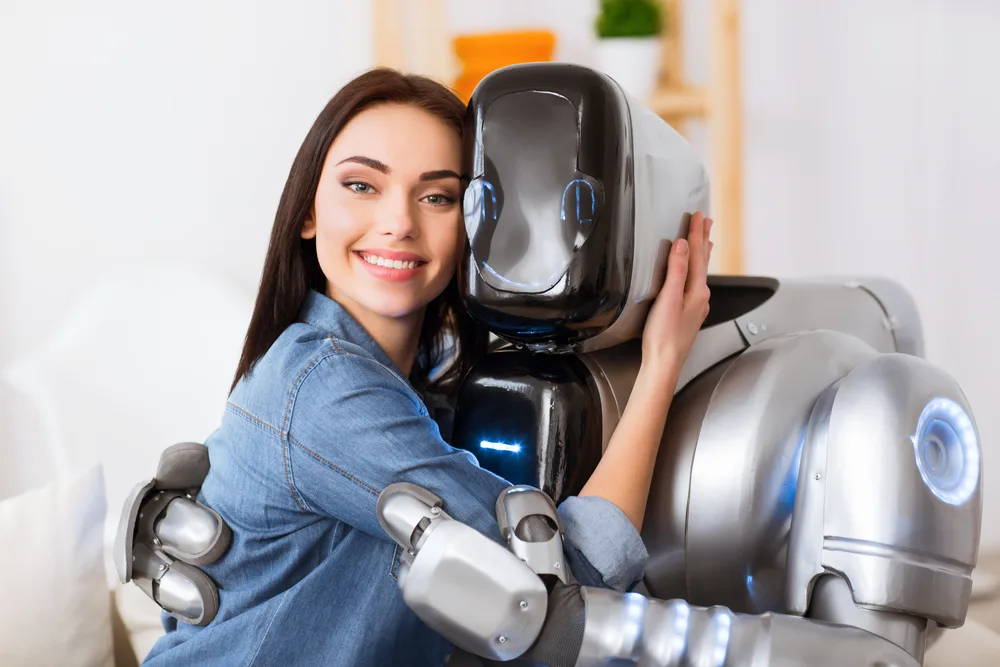 Seize the moment. Cheerful delighted beautiful girl sitting on the sofa with robot and expressing joy while embracing