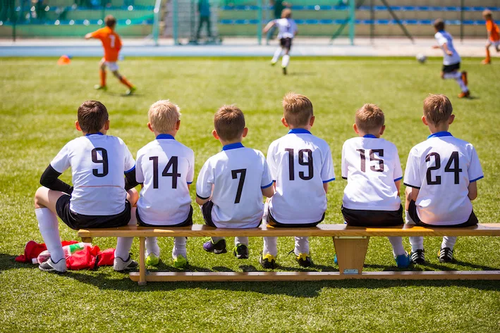 Football soccer match for children. Kids waiting on a bench.
