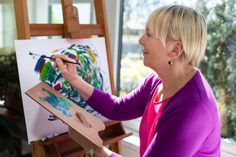 Happy retired woman painting on canvas for fun at home