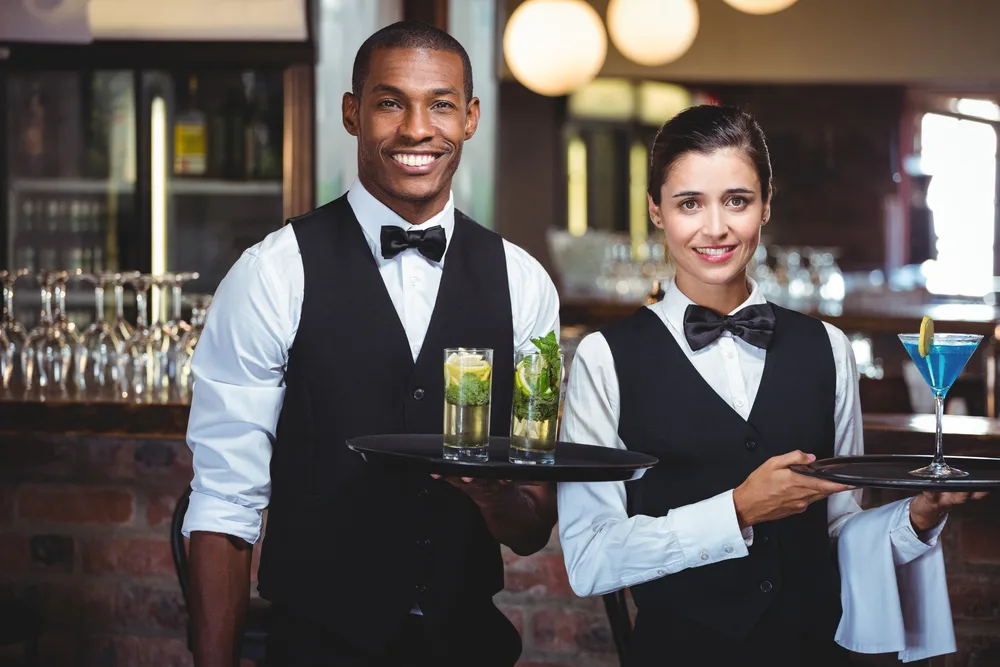 Portrait of waiter and waitress holding a serving tray with glass of cocktail