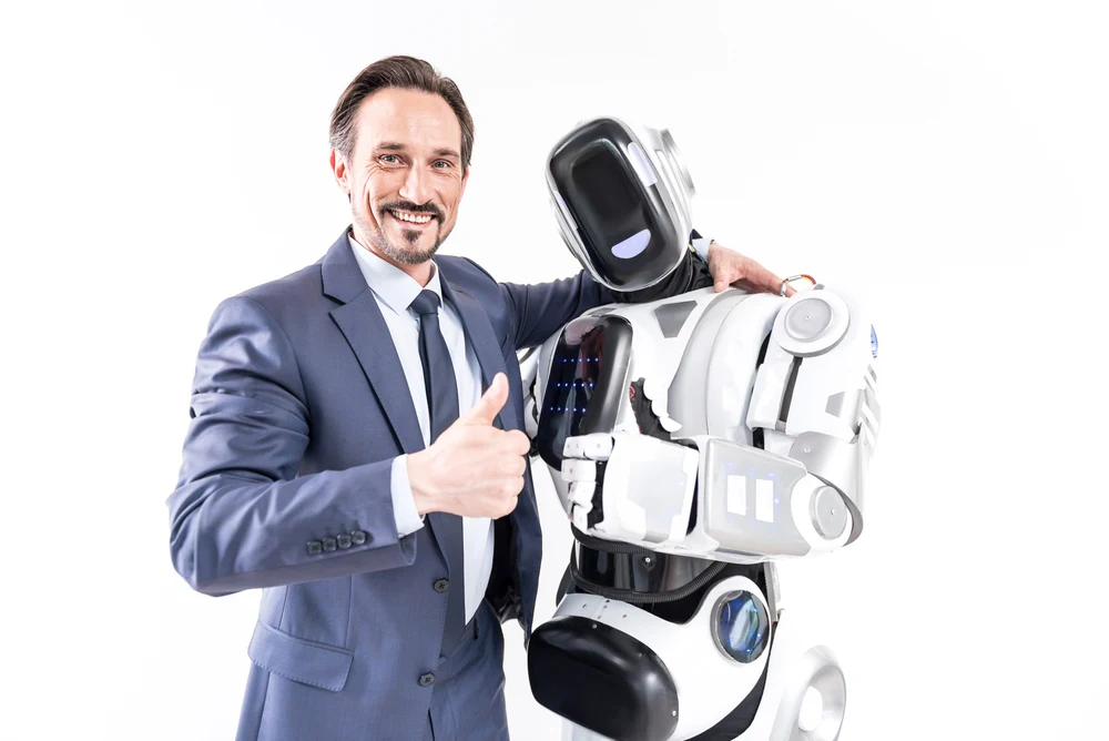 Hilarious man is hugging robot and looking at camera with smile. They showing okay sign. Portrait. Isolated