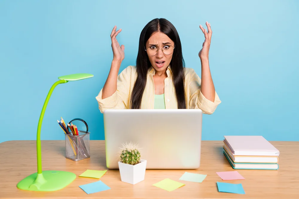 Photo of unhappy worried young woman sit desk problem deadline work laptop isolated on pastel blue color background.