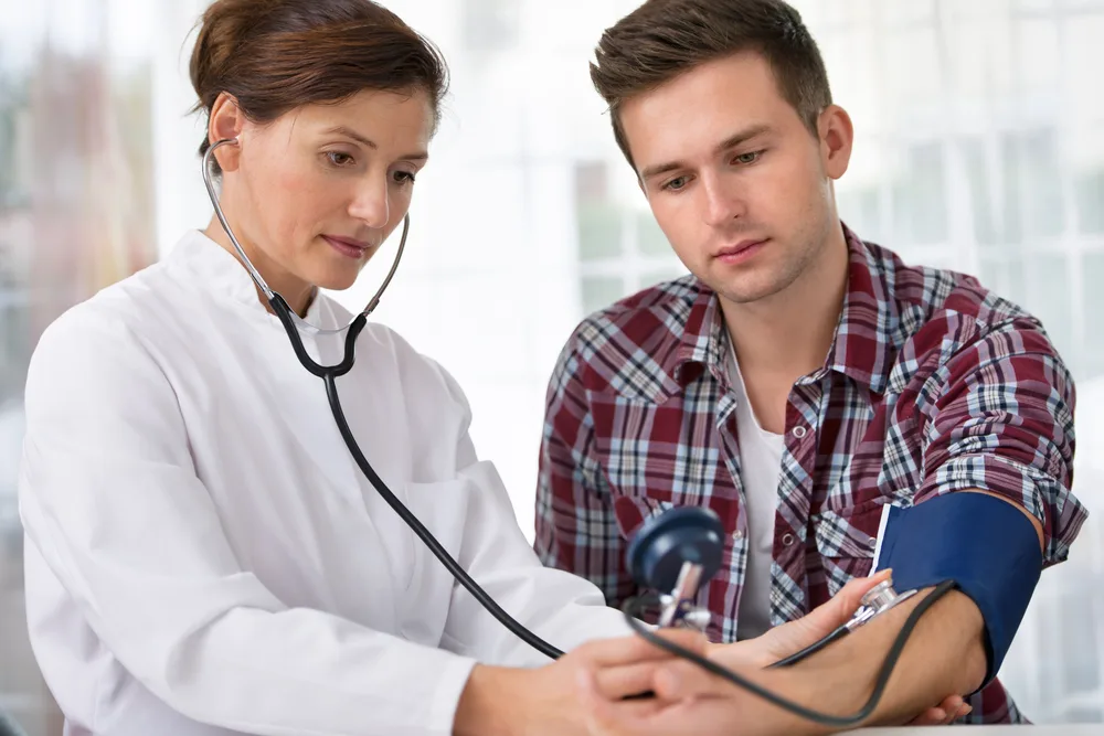 Female doctor checking young man blood pressure 