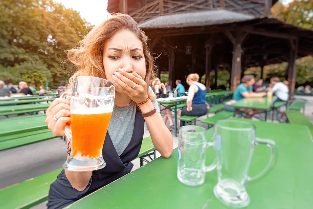 A girl tries a beer with an expression of disgust in a street bar. Concept of alcohol poisoning and quit drinking