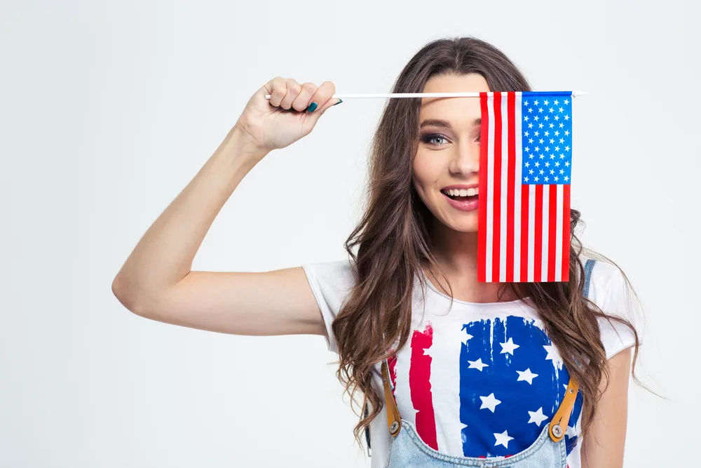 Portrait of a smiling woman covering her eye with USA flag isolated on a white background