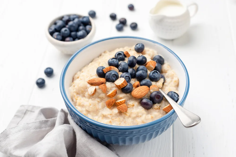 Healthy breakfast oatmeal porridge in bowl with blueberries and almonds on white wooden table background