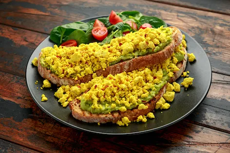 Scrambled Tofu crispy Toast with guacamole and spinach, tomato salad. Vegan vegetarian, plant based food.