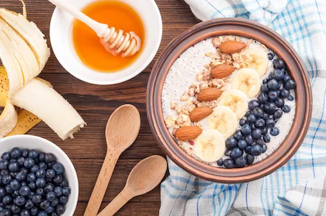 Smoothie bowl with banana, blueberries and almond. Healthy breakfast with yogurt, fruits, nuts and berries on wooden background with copy space. Summer food. Top view