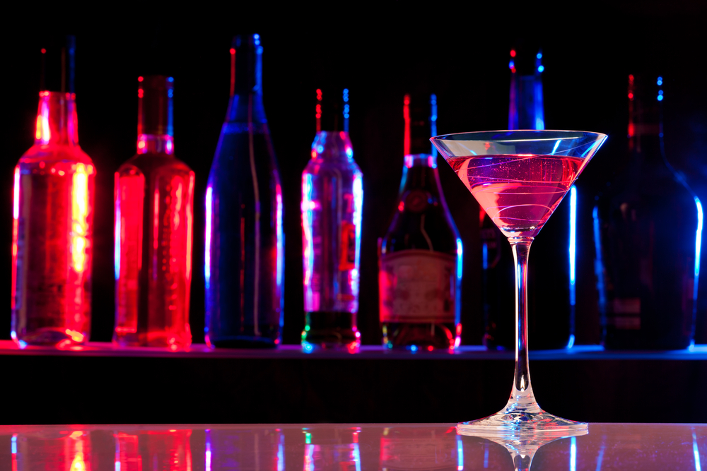 Cocktail glass with drink in the bar with bottles in the dark background