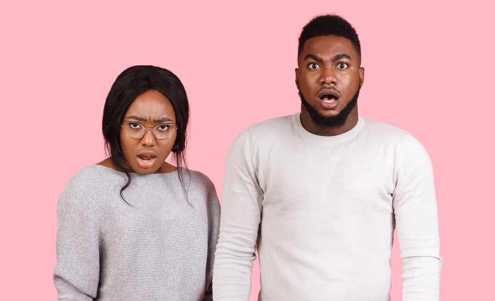 Amazed african man and woman with open mouths looking at camera over pink background