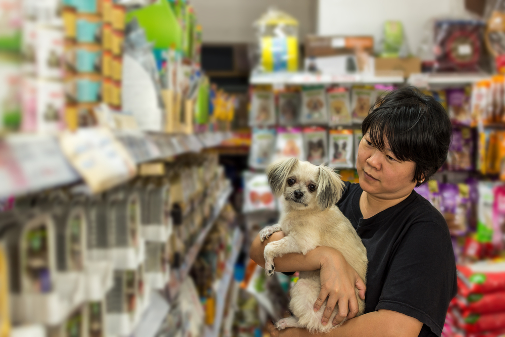 Women and her dog shop a pet food (Dog, Cat and other) on pet goods shelf in pet shop.