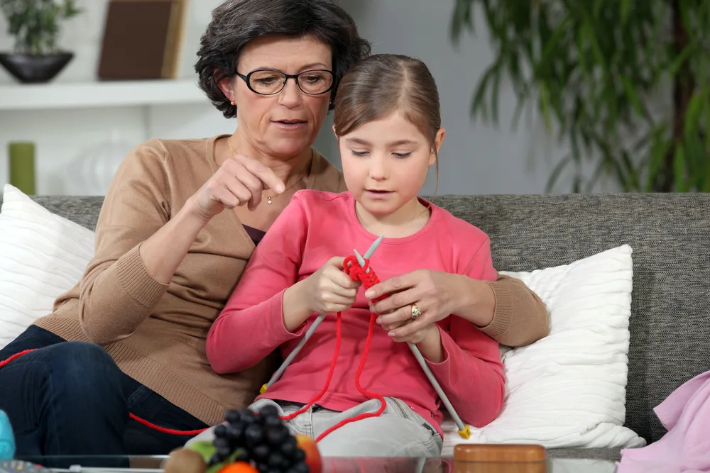Woman teaching how to knit to little girl