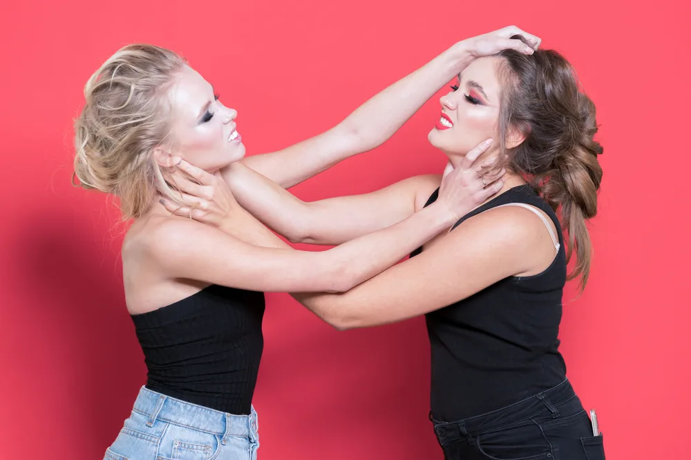 Two girls fighting in the studio on a red background. Negative emotions, expression