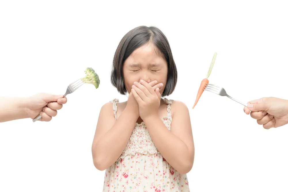 asian child girl with expression of disgust against vegetables isolated on white background, Refusing food concept