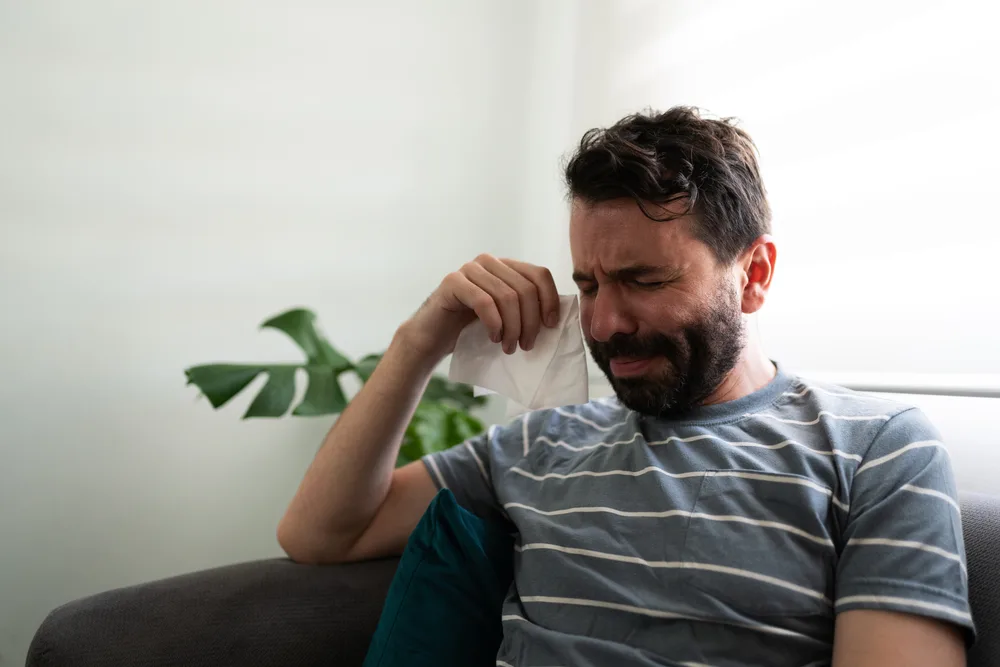 Heartbroken man in his 30s sitting on the couch with a tissue and crying for his break up