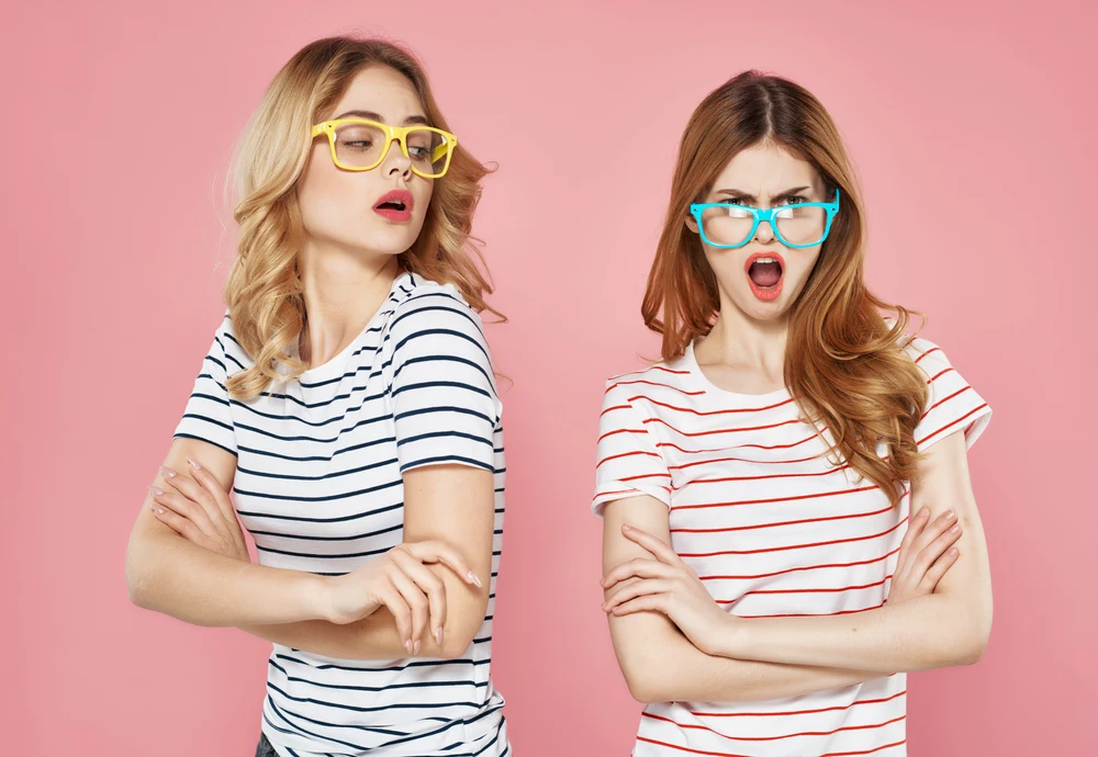 two girlfriends striped t-shirts with sunglasses pink background. High quality photo