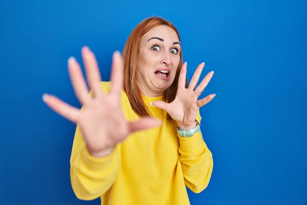 Young woman standing over blue background afraid and terrified with fear expression stop gesture with hands, shouting in shock. panic concept.