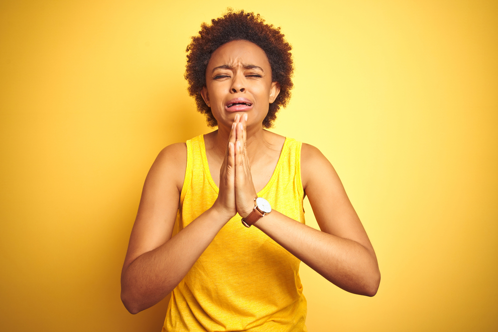 Beauitul african american woman wearing summer t-shirt over isolated yellow background begging and praying with hands together with hope expression on face very emotional and worried. Asking for forgiveness. Religion concept.