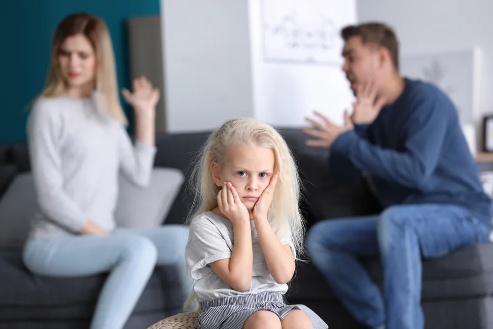 Sad little girl in room with quarreling parents. Family conflict