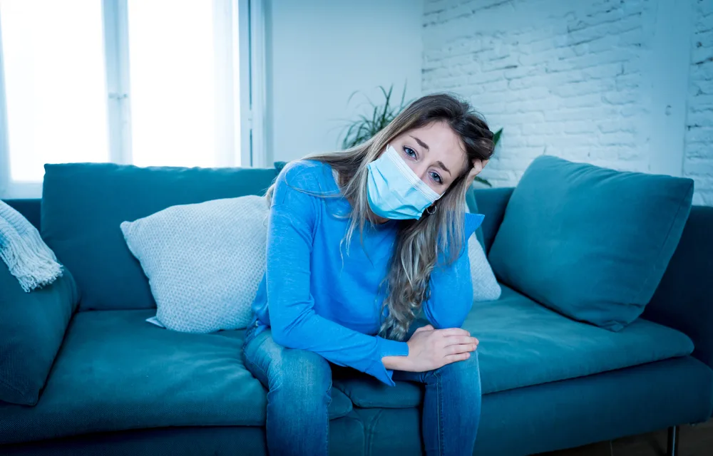 Sad,Woman,With,Protective,Face,Mask,At,Home,Living,Room