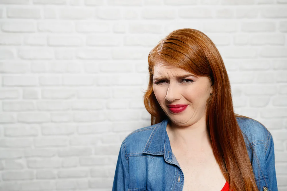 Portrait of disgusted woman, hispanic redhead girl showing disgust for bad smell or taste. Copy space