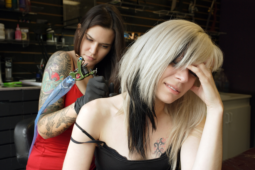 A female tattoo artist applying her craft onto the back and arm of a female in her 30's. (Property release for tattoo artwork attached)