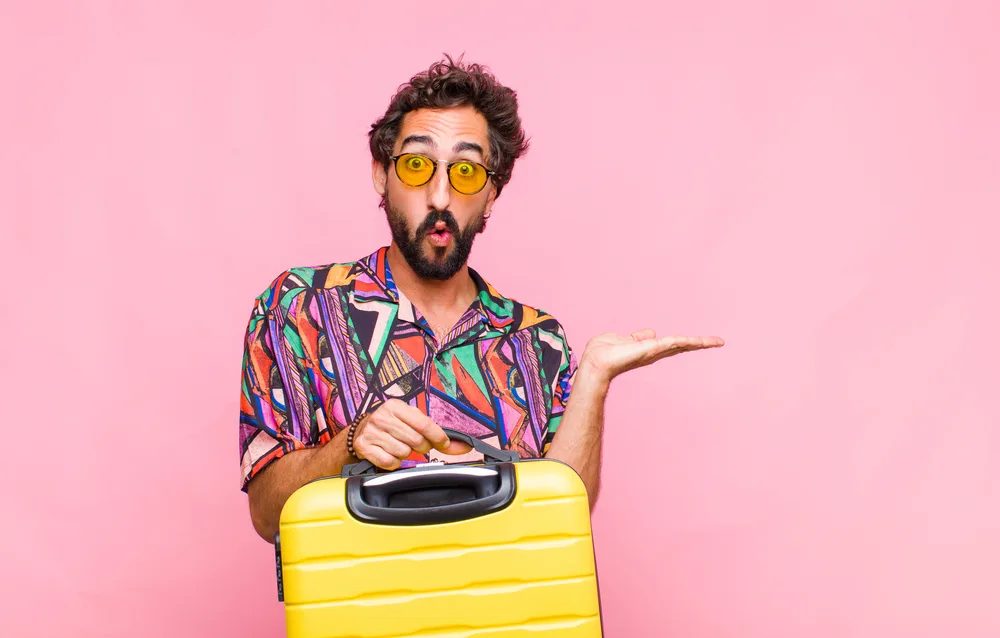 young bearded man looking surprised and shocked, with jaw dropped holding an object with an open hand on the side