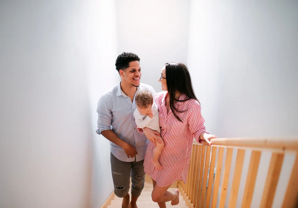 A portrait of young family with small toddler son indoors at home, walking up the stairs.