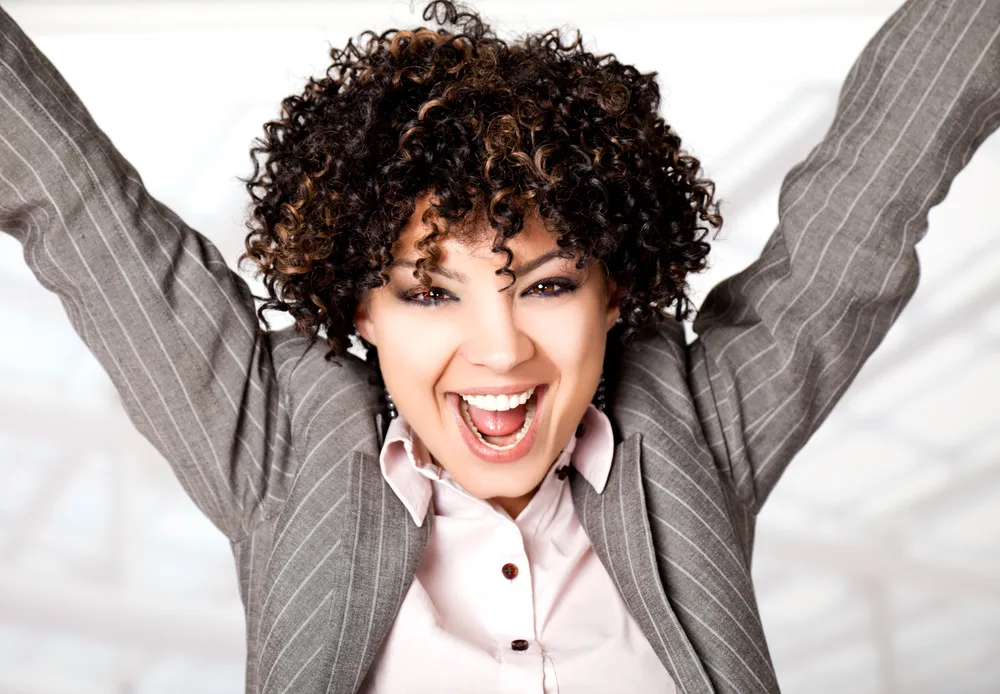 Beautiful happy woman with corly hair raising her arms with excitement.
