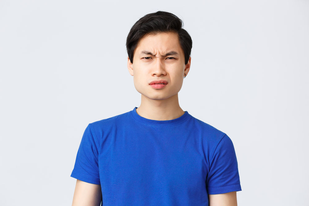 Lifestyle, people emotions and beauty concept. Wtf going on. Frustrated and puzzled asian guy in blue t-shirt frowning, grimacing confused cant understand what happened, stand grey background.